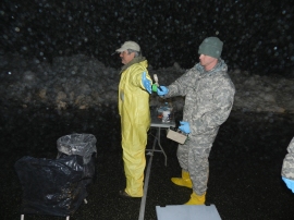 As snow falls, Sgt. Ryan Wickenden, health physics NCO on Nuclear Disablement Team – 3 clears collection team member Don Dale, Department of Energy, through the contamination control line during Prominent Hunt 13-2.  The exercise was a Department of Homeland Security led event in N.Y. that 20th Spt. Cmd. (CBRNE) participated in, along with other agencies in mid Feb.